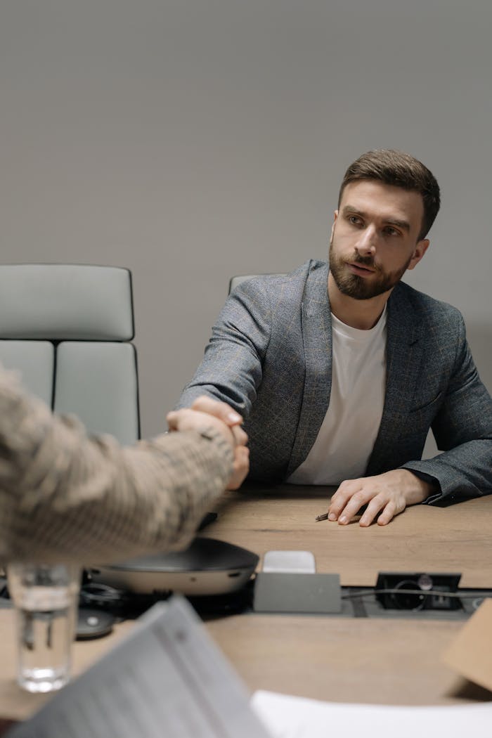 team-02 Two businessmen in a modern office shaking hands across a table. Professional setting.